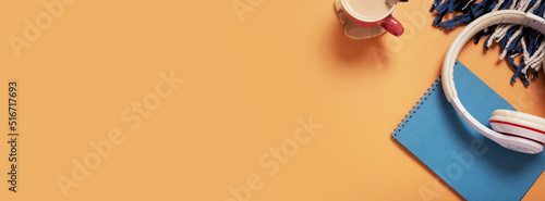 Table with blue paper note pad, coffee cup, headphones and pliad on colored background. Banner with copy space. Top view photo