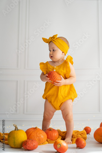 Little girl sits on the floor on a white background. The child is holding an orange pumpkin. Toddler and Halloween in autumn
