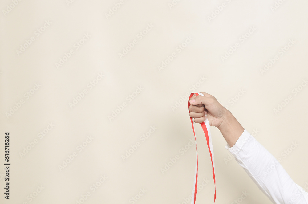 A human hand holds red white ribbon as symbol of the Indonesian flag ...