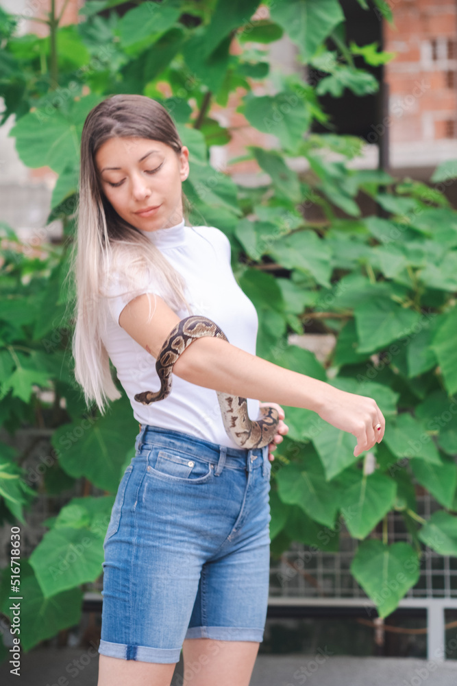 Portrait of a young woman in jeans and a snake by the wild plants in an urban environment Portrait of a young woman in jeans and a snake by the wild plants in an urban environment