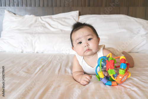 Portrait of cute little asian baby girl wearing white bodysuit lying on white beedsheets and toy at home.