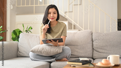 Charming asian woman using digital tablet on couch in cozy living room, enjoying leisure weekend time alone at home