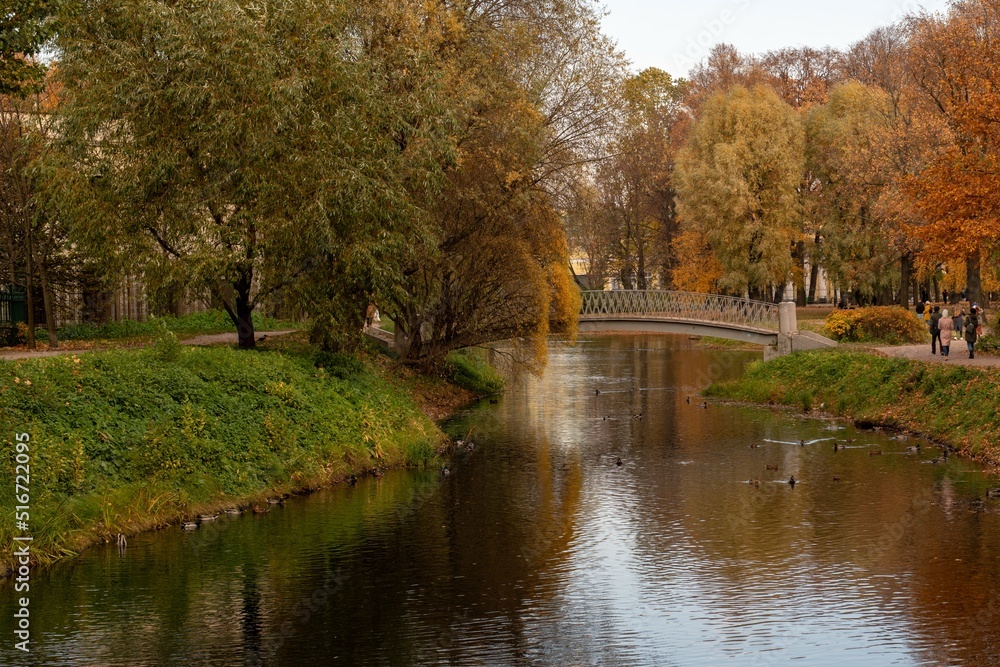 A beautiful bridge over the river in the city park on an autumn day. Autumn in the city park. Yellow and red trees on the bank of the river A beautiful bridge over the river in the city park on an autumn day. Autumn in the city park. Yellow and red trees on the bank of the river