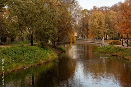 A beautiful bridge over the river in the city park on an autumn day. Autumn in the city park. Yellow and red trees on the bank of the river