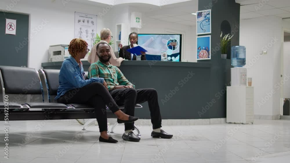 African american man and woman talking about disease in hospital reception lobby, waiting to attend consultation appointment with specialist. Patients in waiting area. Tripod shot. African american man and woman talking about disease in hospital reception lobby, waiting to attend consultation appointment with specialist. Patients in waiting area. Tripod shot.