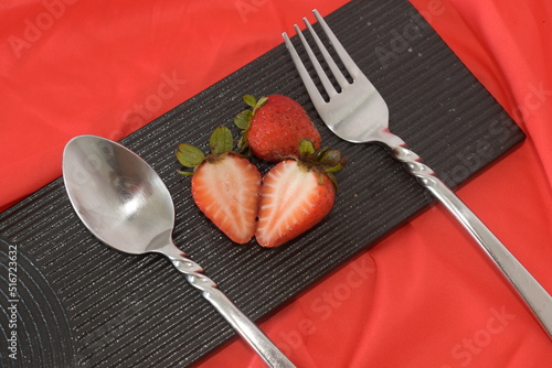vivid red strawberry on black ceramic dish on red background with silverware