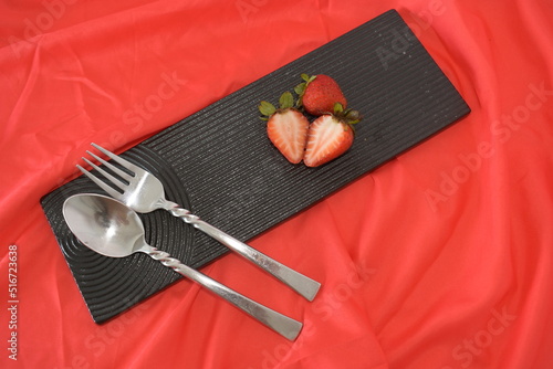 vivid red strawberry on black ceramic dish on red background