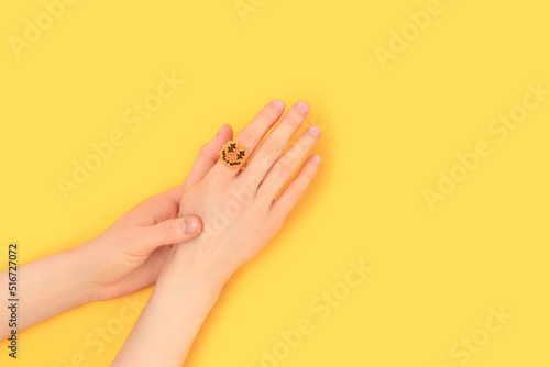 Female hands with smiley ring made of beads on a yellow background. Place for text.