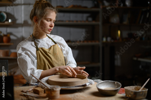 A ceramist makes a plate. Woman in an apron works in a pottery workshop. 