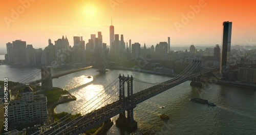 Lively traffic over Manhattan Bridge at Golden hour. Gorgeous skyscraper’s silhouettes at backdrop of orange skies. Top view.