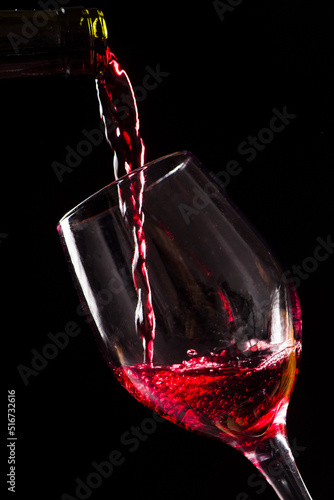 Red wine being poured into wine glass on black background.