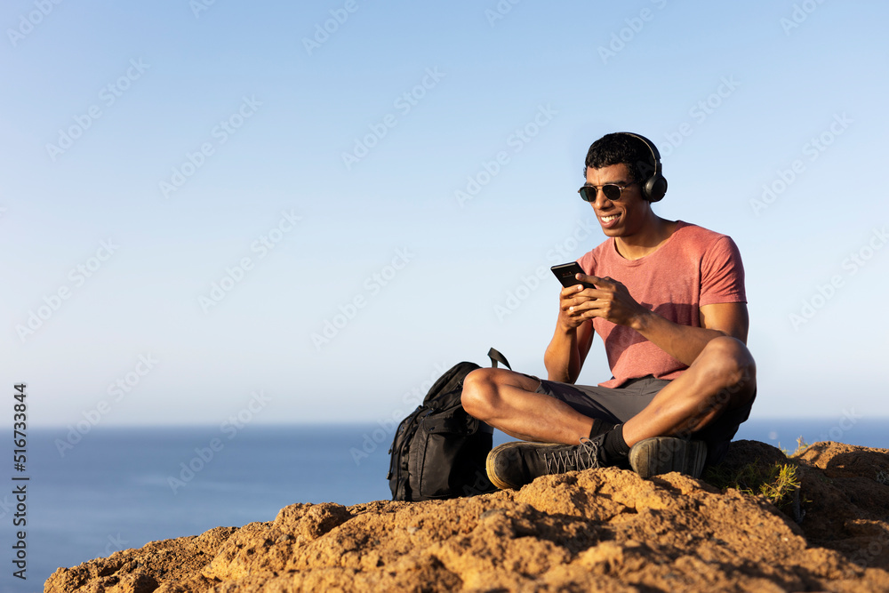 Young man sitting on the stone listening the music. Tourist man on the top of the mountain..