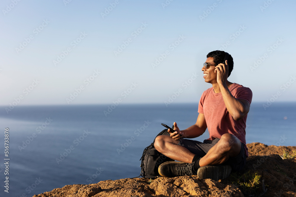 Young man sitting on the stone listening the music. Tourist man on the top of the mountain..