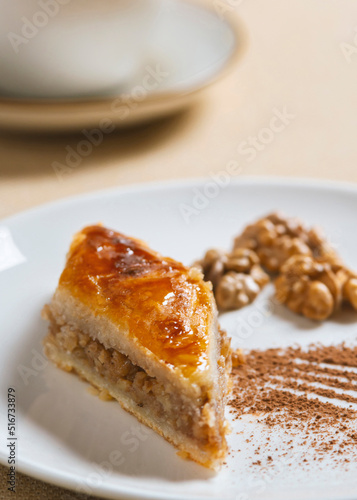 Traditional arabic dessert baklava and walnuts in white plate with a cup of coffee or tea .Homemade baklava with nuts and honey.