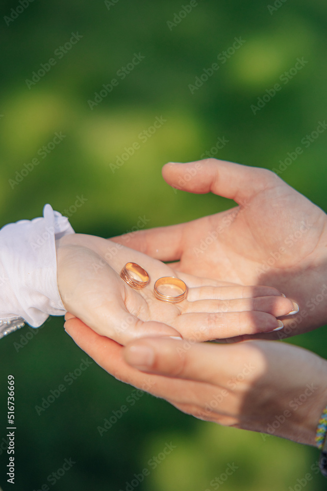 Hands of groom hold hand of bride with golden rings.