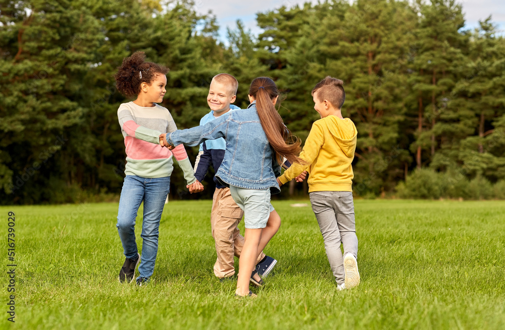 Fototapeta premium childhood, leisure and people concept - group of happy kids playing round dance at park