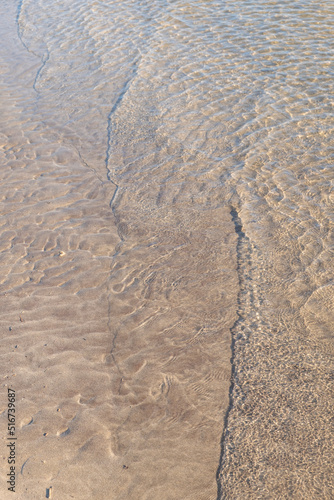 Detail close-up of wave washing onto sand beach shoreline, summer concept