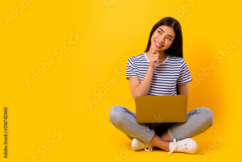 Full body portrait of charming cheerful lady sit floor hand touch chin look empty space hold netbook isolated on yellow color background