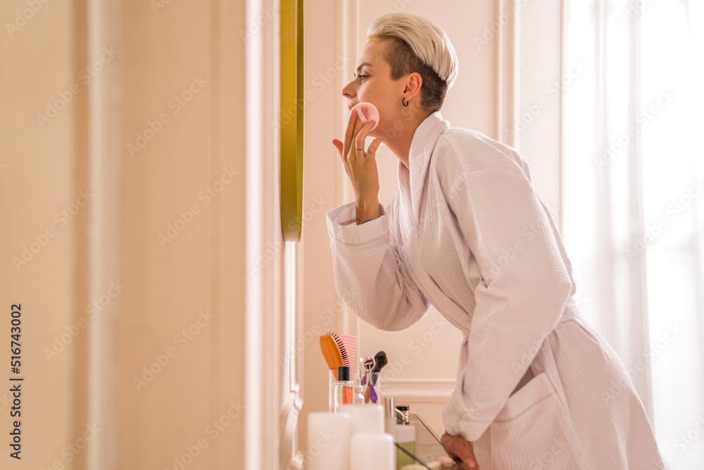 Female wearing white bathrobe using cotton pads while remove make up from her face Female wearing white bathrobe using cotton pads while remove make up from her face