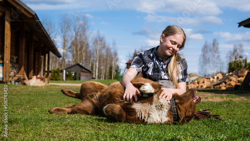 A teenage girl plays with a dog in the yard on a sunny day. Happiness.