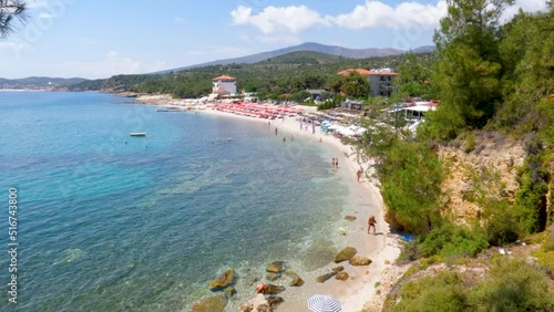 Panoramic view of turquoise clear sea water, organized beach, sand and pebbles , tourists on the beach on a summer day. Pine trees surround the beach. Pefkari village, Thasos, Greece. 4K footage. photo