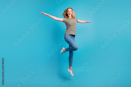 Full size view of nice glad wavy-haired girl jumping having fun rising hands isolated blue color background