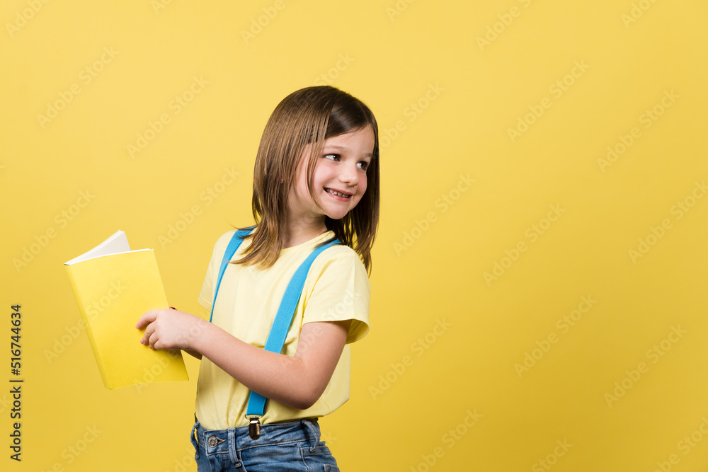 Cheerful little girl holding book and looking back at yellow copy space. Cheerful little girl holding book and looking back at yellow copy space.
