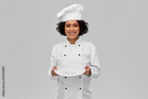 cooking, culinary and people concept - happy smiling female chef in white toque and jacket holding empty plate over grey background