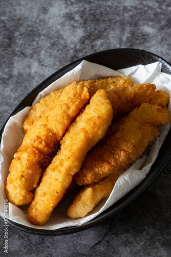 Breaded chicken fillet strips on a paper towel in a black bowl. On a concrete background