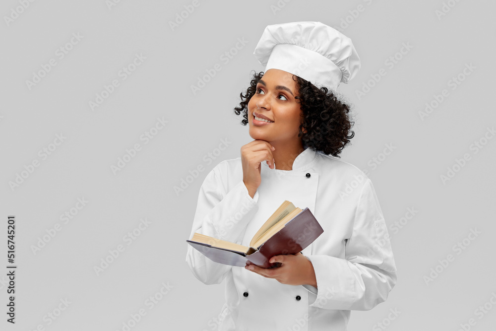 cooking, culinary and people concept - happy smiling female chef in white toque and jacket reading cook book over grey background cooking, culinary and people concept - happy smiling female chef in white toque and jacket reading cook book over grey background