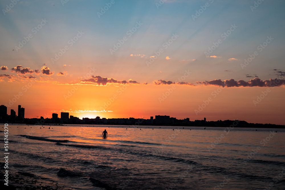 The sunrise seen from the postiguet beach in Alicante, with buildings and people against the light. The sunrise seen from the postiguet beach in Alicante, with buildings and people against the light.