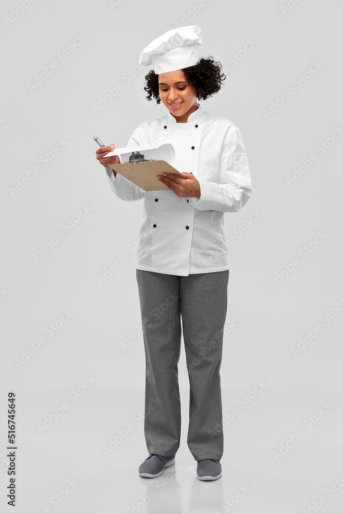 cooking, culinary and people concept - happy smiling female chef in toque and jacket with papers on clipboard over grey background cooking, culinary and people concept - happy smiling female chef in toque and jacket with papers on clipboard over grey background