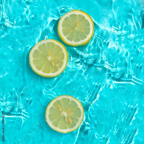 Lemon slices in water blue background with copy space. Water splashing. Summer, vacation, food concept. Top view. 