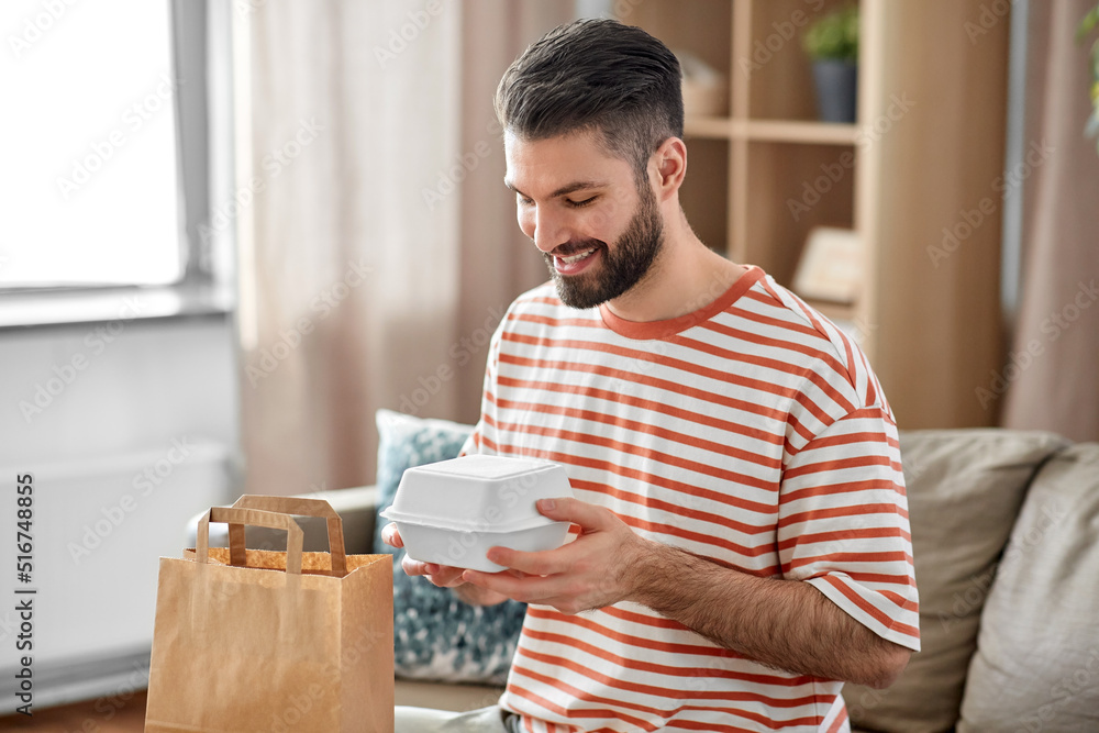 consumption, eating and people concept - smiling man unpacking takeaway food in paper bag at home consumption, eating and people concept - smiling man unpacking takeaway food in paper bag at home