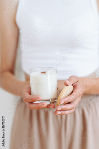 Woman in Home Clothes Holds White Candle with Wooden Lid in Her Hands. Blurred Background