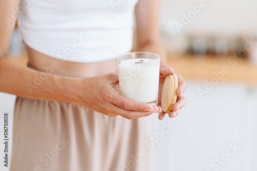 Woman holds in her Hands White Candle with Wooden Lid. Blurred Background.