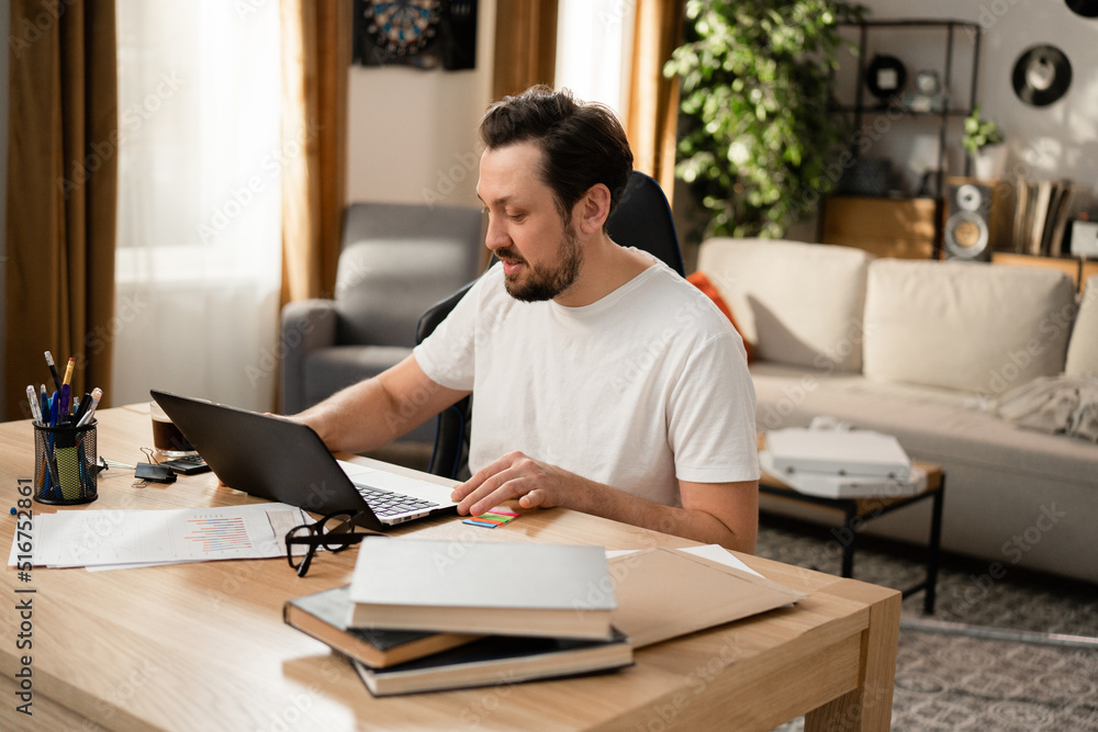 Brunette sitting at table and working on laptop. Today he successfully completed project. A cup of coffee cheered him up and sunny day added to good mood. Brunette sitting at table and working on laptop. Today he successfully completed project. A cup of coffee cheered him up and sunny day added to good mood.