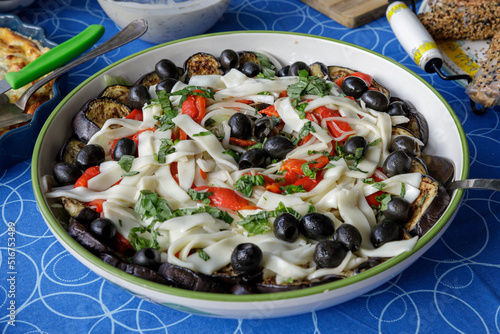 long pasta salad with black olives, fried eggplant slices, red pepper and green leaves