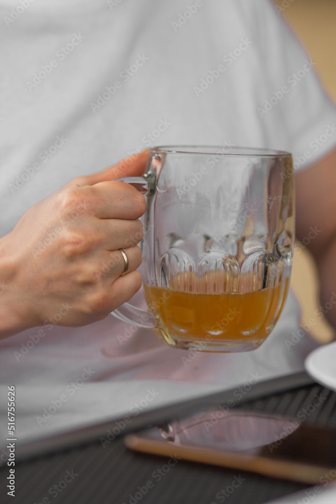 Man's hand holding a glass of beer. Married man in white t-shirt drinking tasty beer in pub. Man's hand holding a glass of beer. Married man in white t-shirt drinking tasty beer in pub.