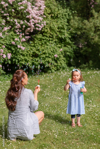 family  motherhood and people concept - happy mother with little daughter blowing soap bubbles at summer park or garden