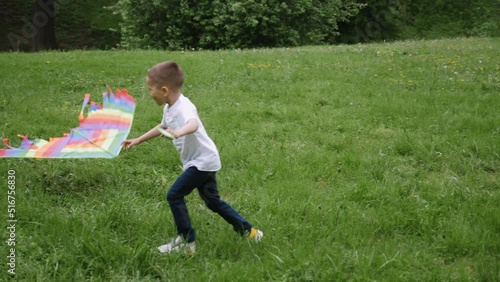 boy child launches a kite running through a green field in the park in summer