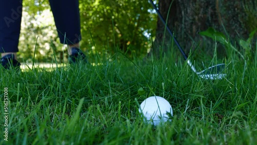 Golf Ball Lying on the Rough Grass and Golfer with Golf Club Searching for Her Golf Ball in the Trees and Picking Up the Ball in a Sunny Day in Switzerland.