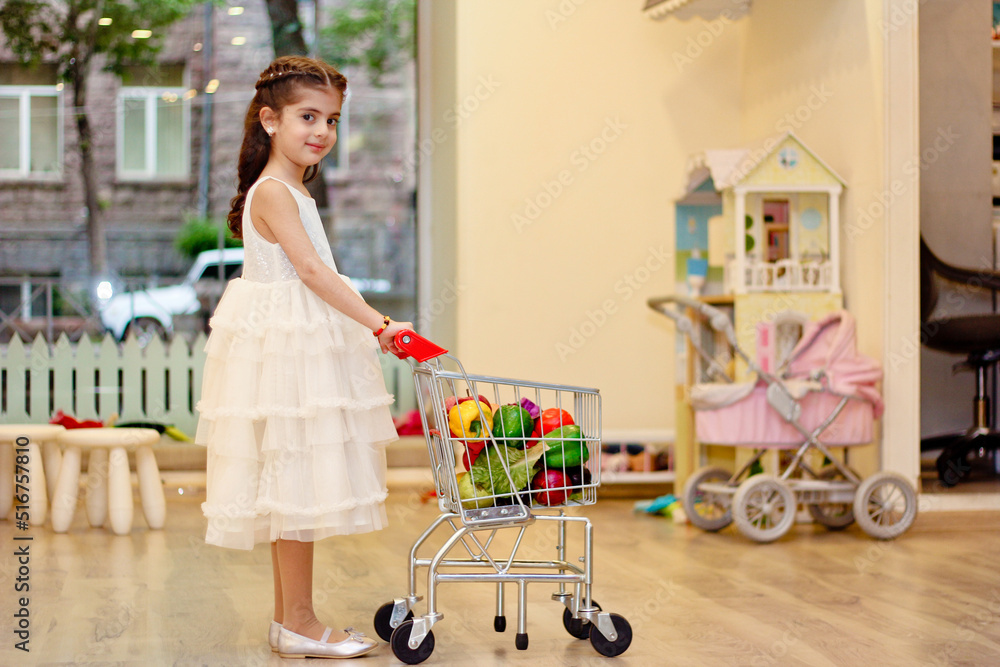 Little girl playing in kindergarten. Holding supermarket basket with artificial fruits