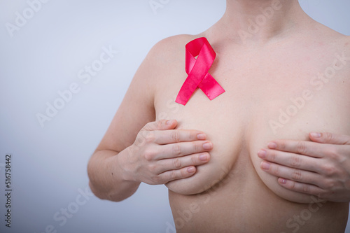 Pink breast cancer awareness ribbon on the chest of a naked woman on a white background.