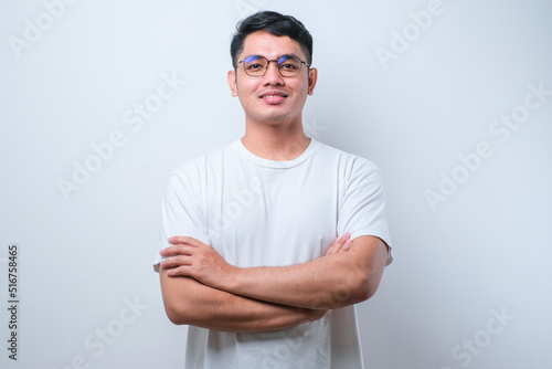 Potrait of young handsome Asian man wearing casual shirt and glasses, happy face smiling with crossed arms looking at the camera
