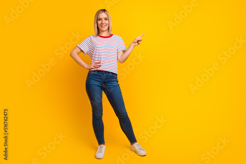 Photo of charming sweet young woman dressed shirt smiling pointing finger empty space isolated yellow color background © Tetiana