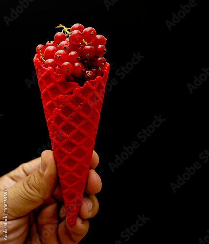 red cone with ice cream decorated with red currant isolated on black background photo