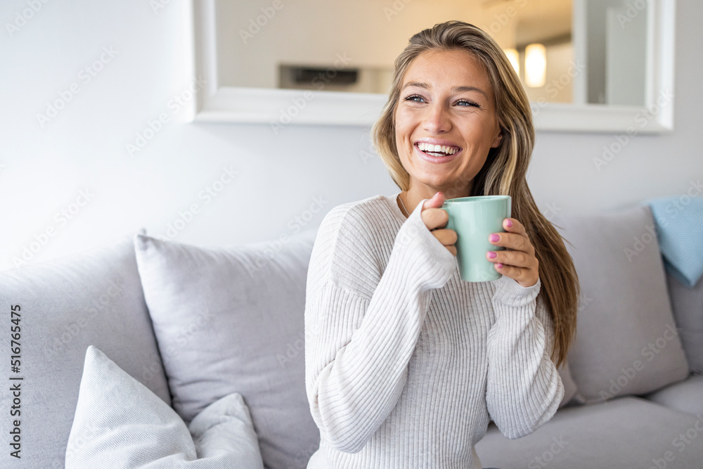 Happy young woman drinking a cup of tea in an autumn morning. Dreaming girl sitting in living room with cup of hot coffee enjoying. Pretty woman wearing sweater at home and enjoy Happy young woman drinking a cup of tea in an autumn morning. Dreaming girl sitting in living room with cup of hot coffee enjoying. Pretty woman wearing sweater at home and enjoy