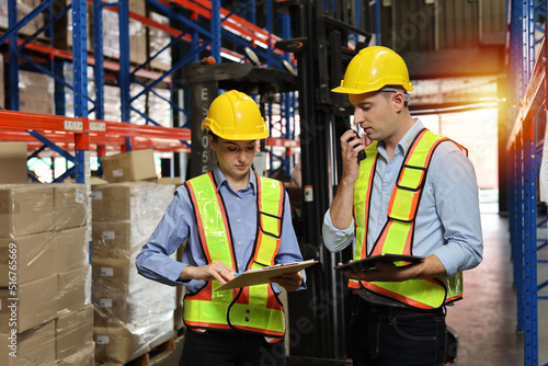 Group of warehouse workers with hardhats and reflective jackets using tablet, walkie talkie radio and cardboard while controlling stock and inventory in retail warehouse logistics, distribution center