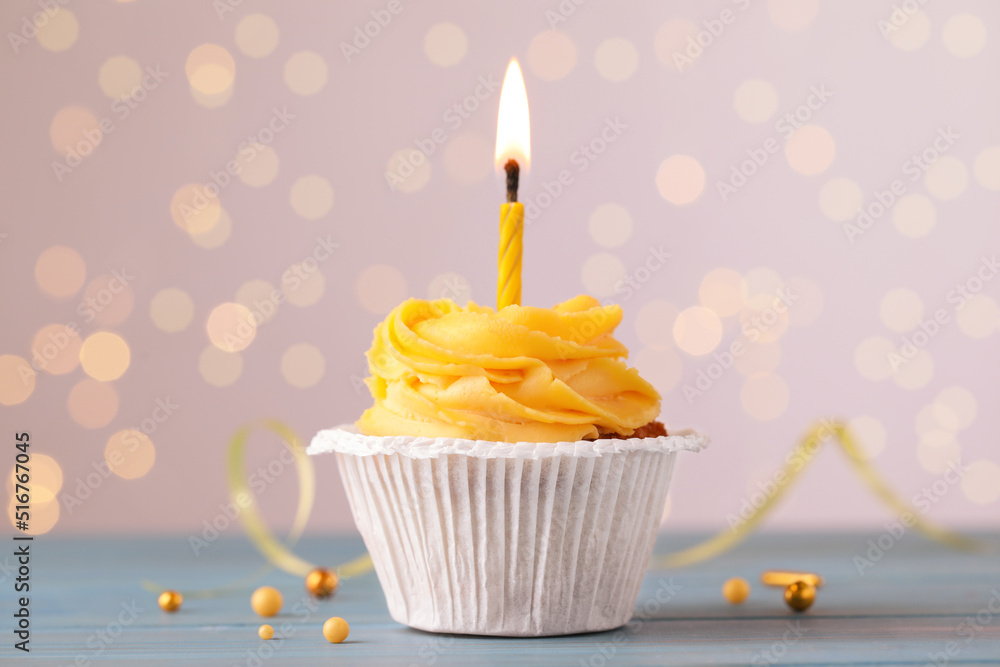 Tasty birthday cupcake on light blue wooden table against blurred lights Tasty birthday cupcake on light blue wooden table against blurred lights